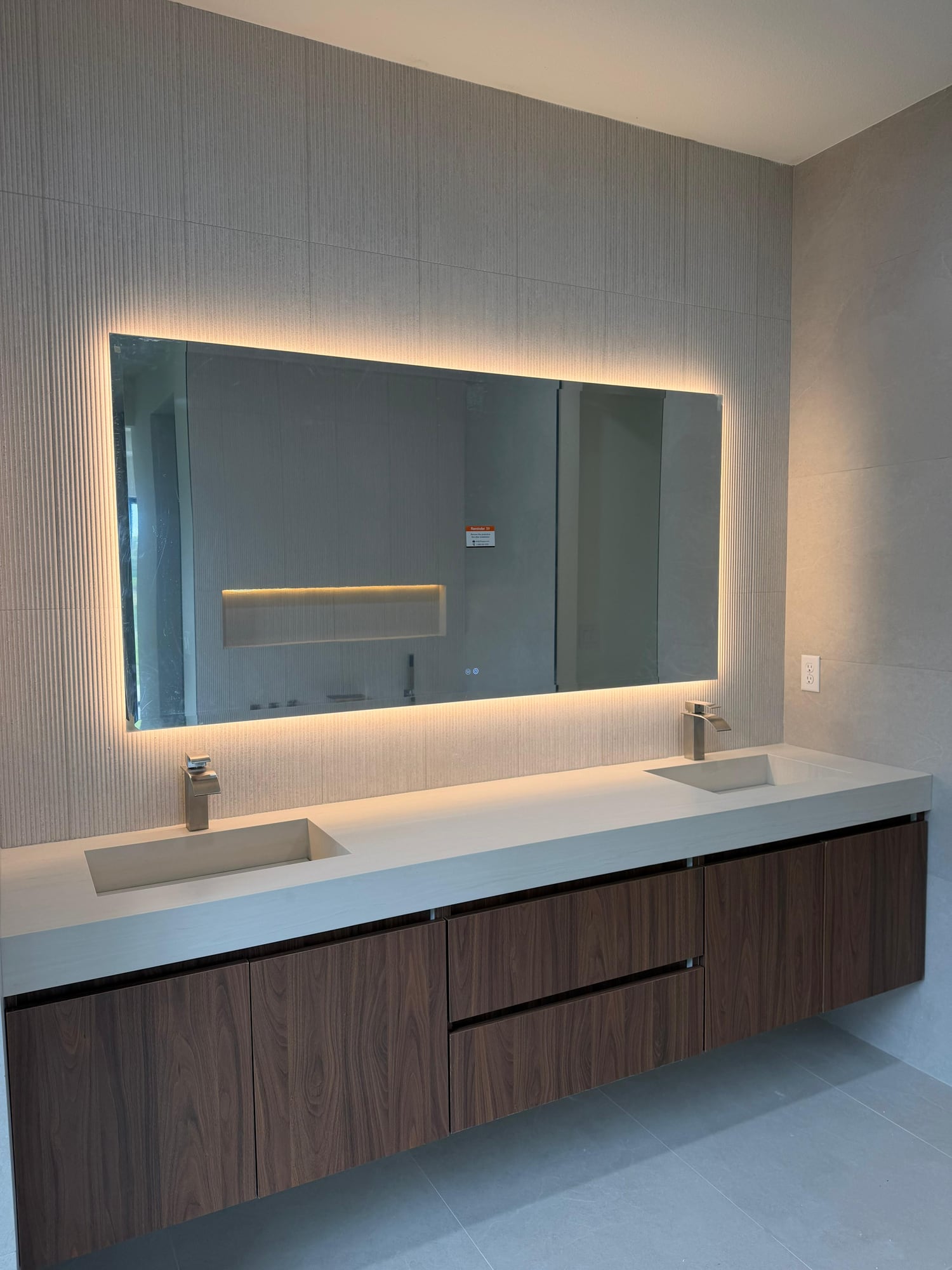 Double bathroom vanity with a pale countertop, wood cabinetry and an illuminated mirror