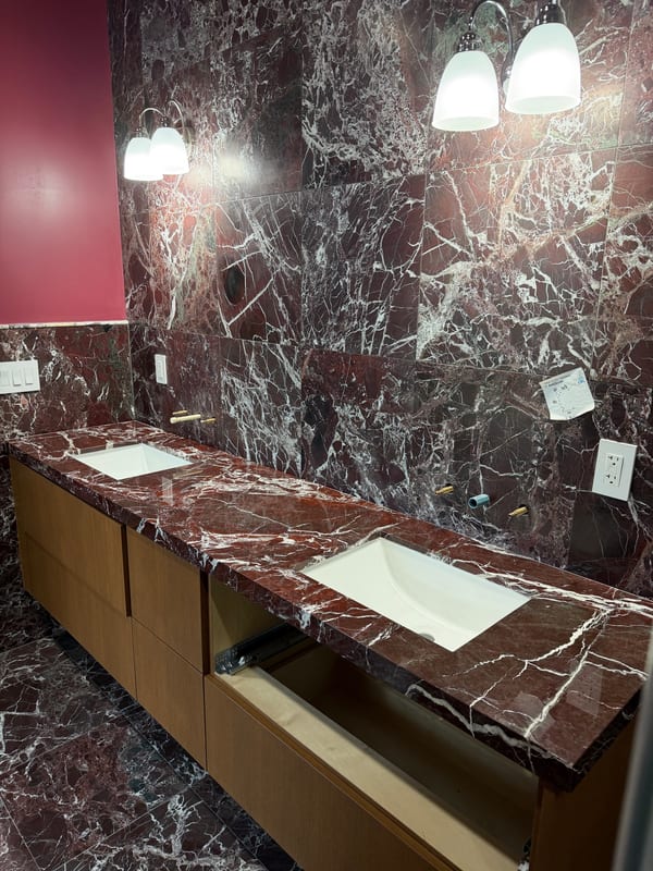 Burgundy marble double vanity with white undermount basins, matching wall cladding and wood cabinets during installation