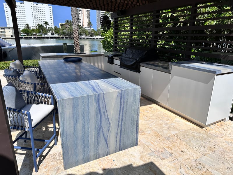 Blue-grey veined outdoor island with chairs in a waterfront setting