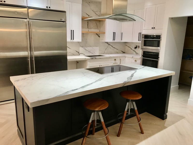 White porcelain kitchen island with a cooktop, two stools and matching full-height backsplash